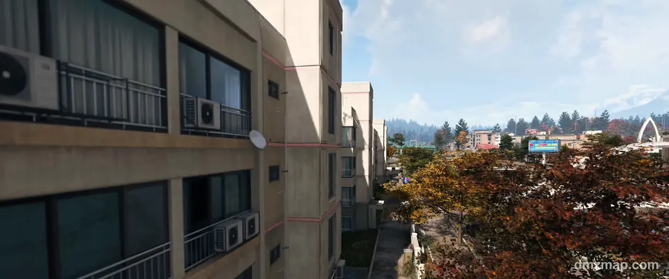 A Hajin apartment block beside a lane of red and orange autumn trees, with a billboard, an arch and snowy mountains in the distance, MW4 DMZ